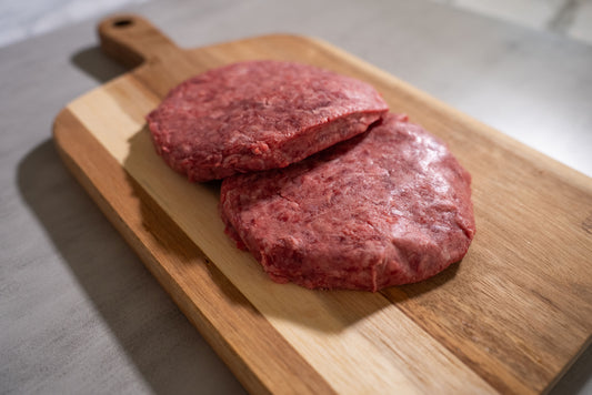 2 Halal Burger Patties one resting ontop of another on a butcher block cutting board with its shadow of the burgers going in the South West 