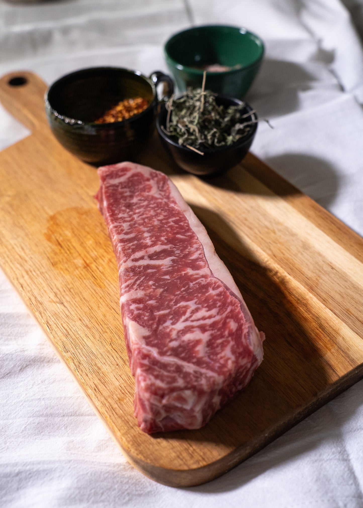Raw steak on a wooden cutting board with spices in small bowls.